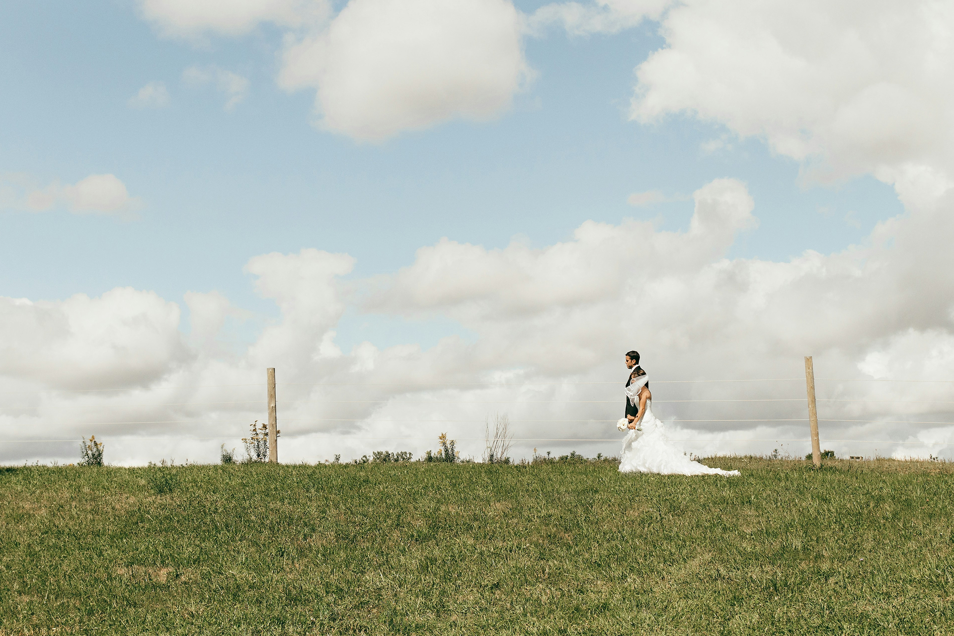 Bride and groom in an open green field beneath a blue sky